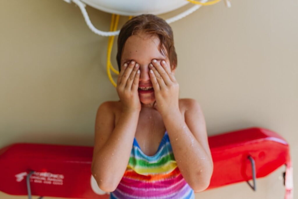 Child in swimming costume hiding eyes with hands