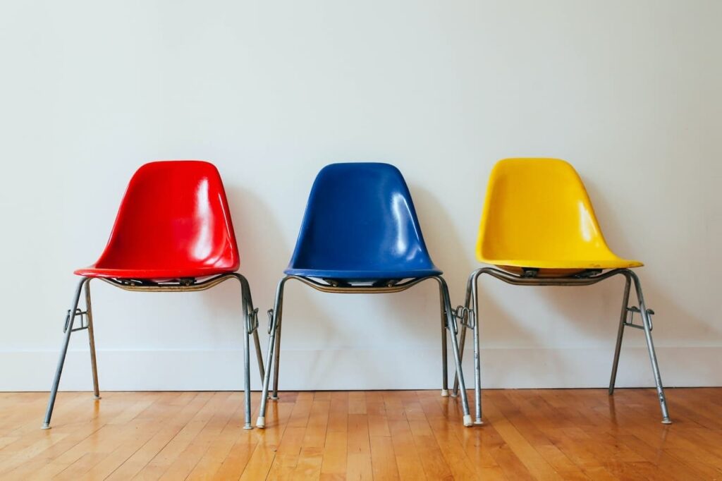 Three brightly coloured plastic chairs in a row, one red, one blue, one yellow