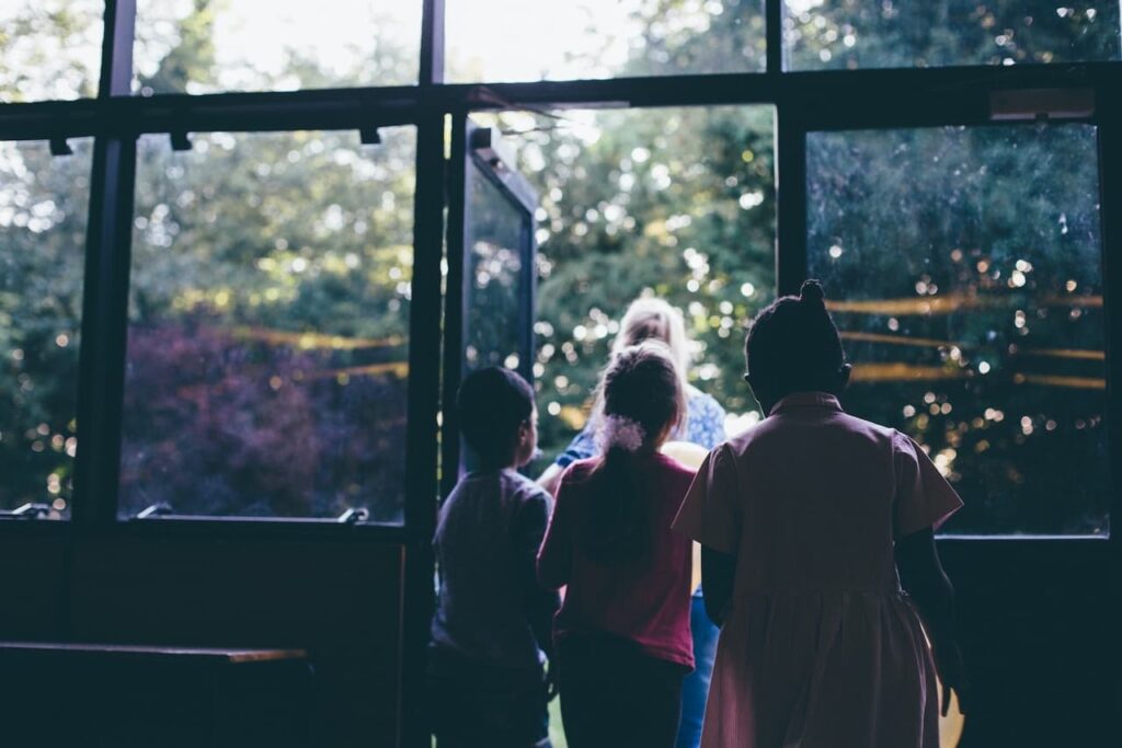 three children following a teacher through a door to the outside