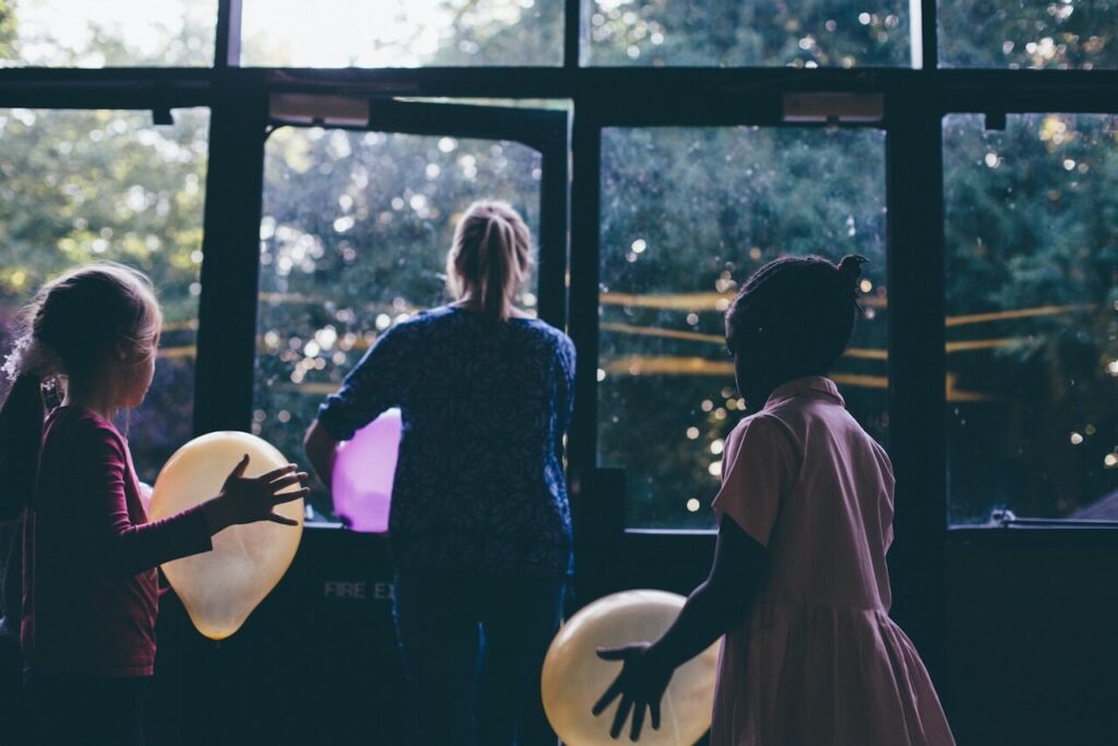 Children holding balloons following a teacher outside